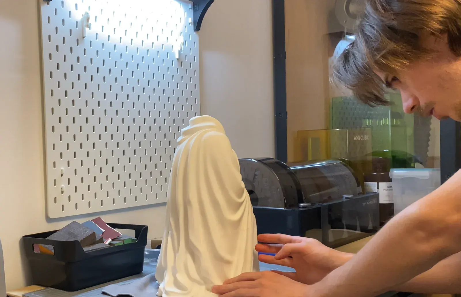 Robin Pellerin ajuste une pièce imprimée en 3D sur son plan de travail, devant les imprimantes de l'atelier SCULPTA à Grenoble