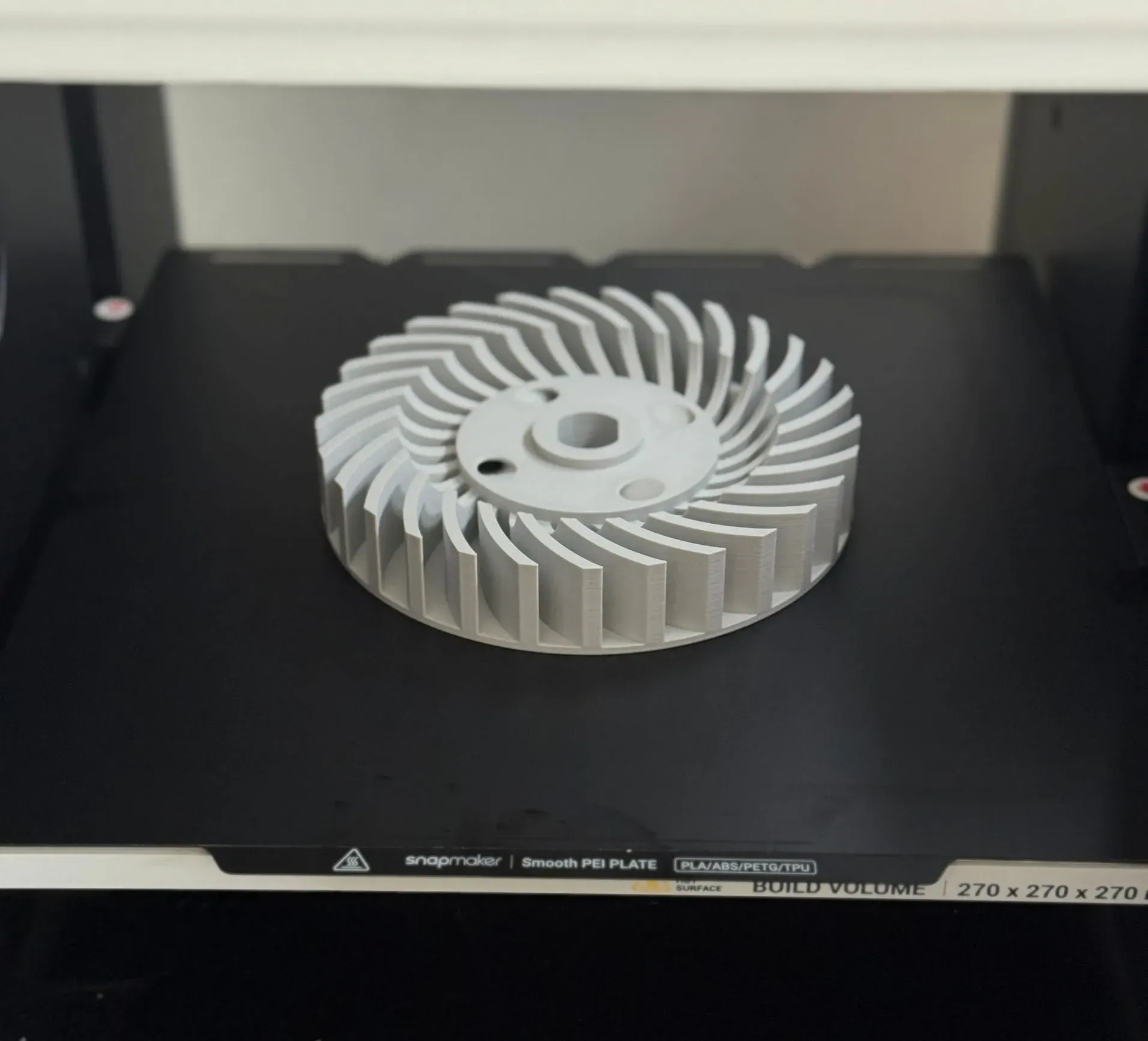 Turbine de ventilation imprimée en 3D en filament gris, sur le plateau de l'imprimante