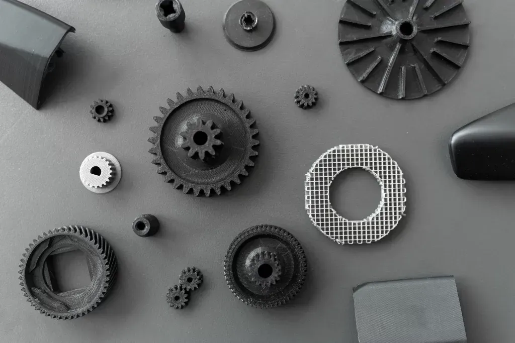 Pièces imprimées en 3D en filament noir et gris sur fond gris : engrenages, hélice et disque à remplissage en treillis